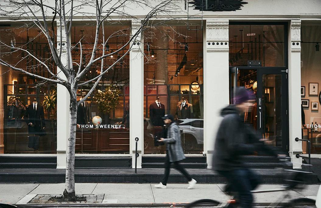 People walking past a store with large windows displaying 'Thom Sweeney'.