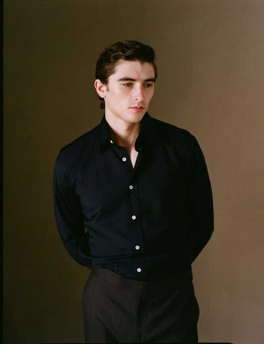 Man wearing a navy shirt with white buttons against a brown background