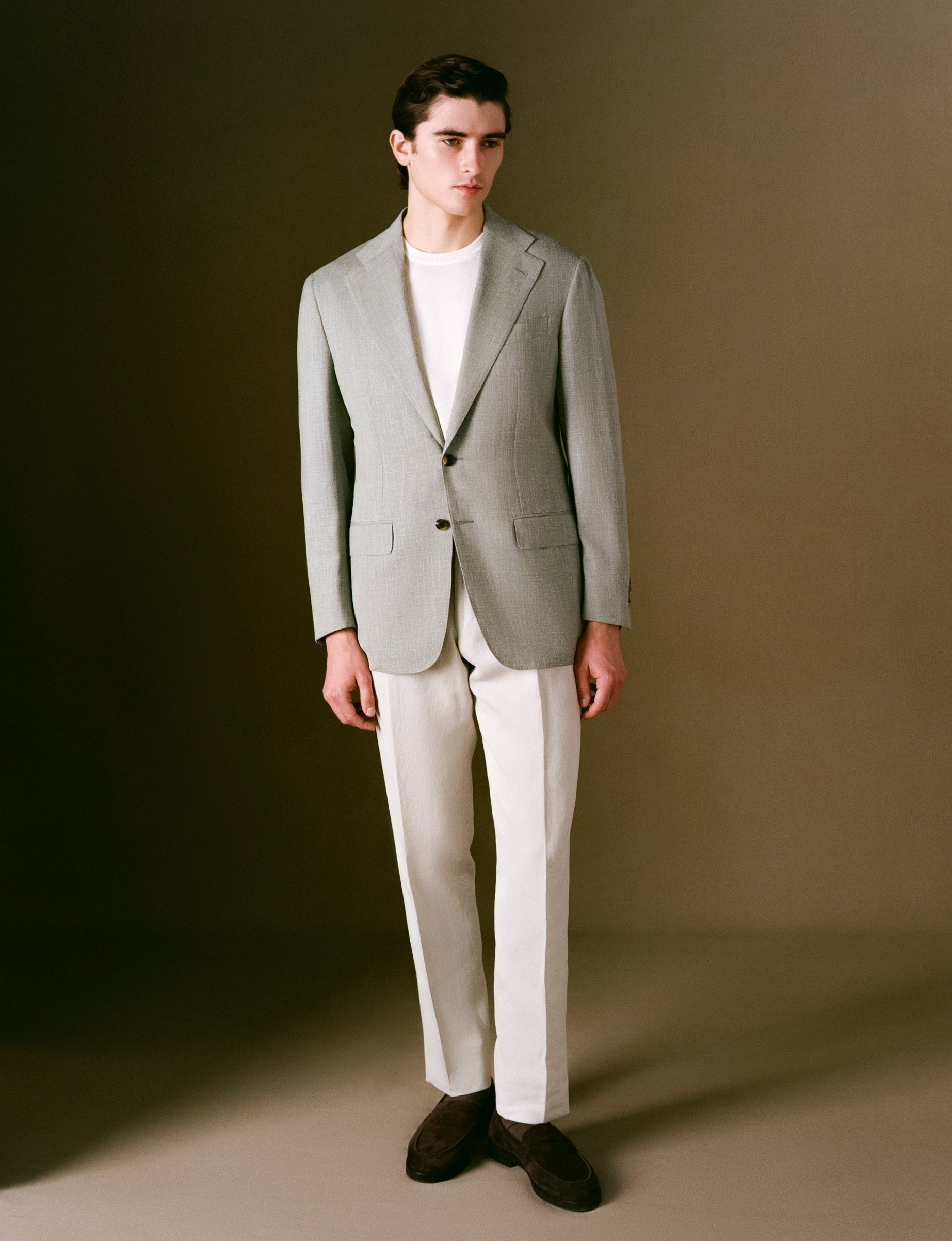 Model in a light sage suit jacket with a white shirt against a brown background