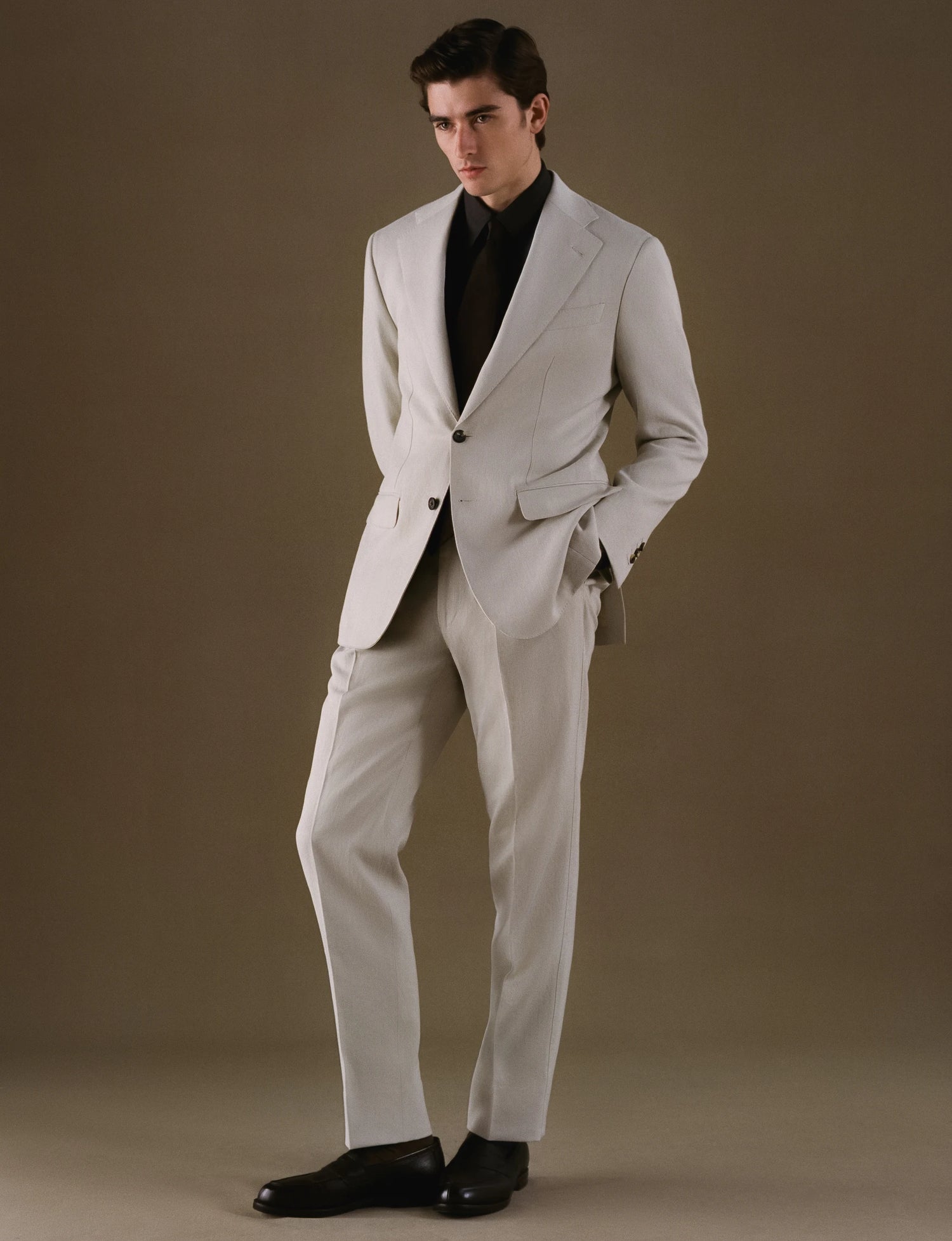 Man wearing a light gray suit with a black shirt against a plain background