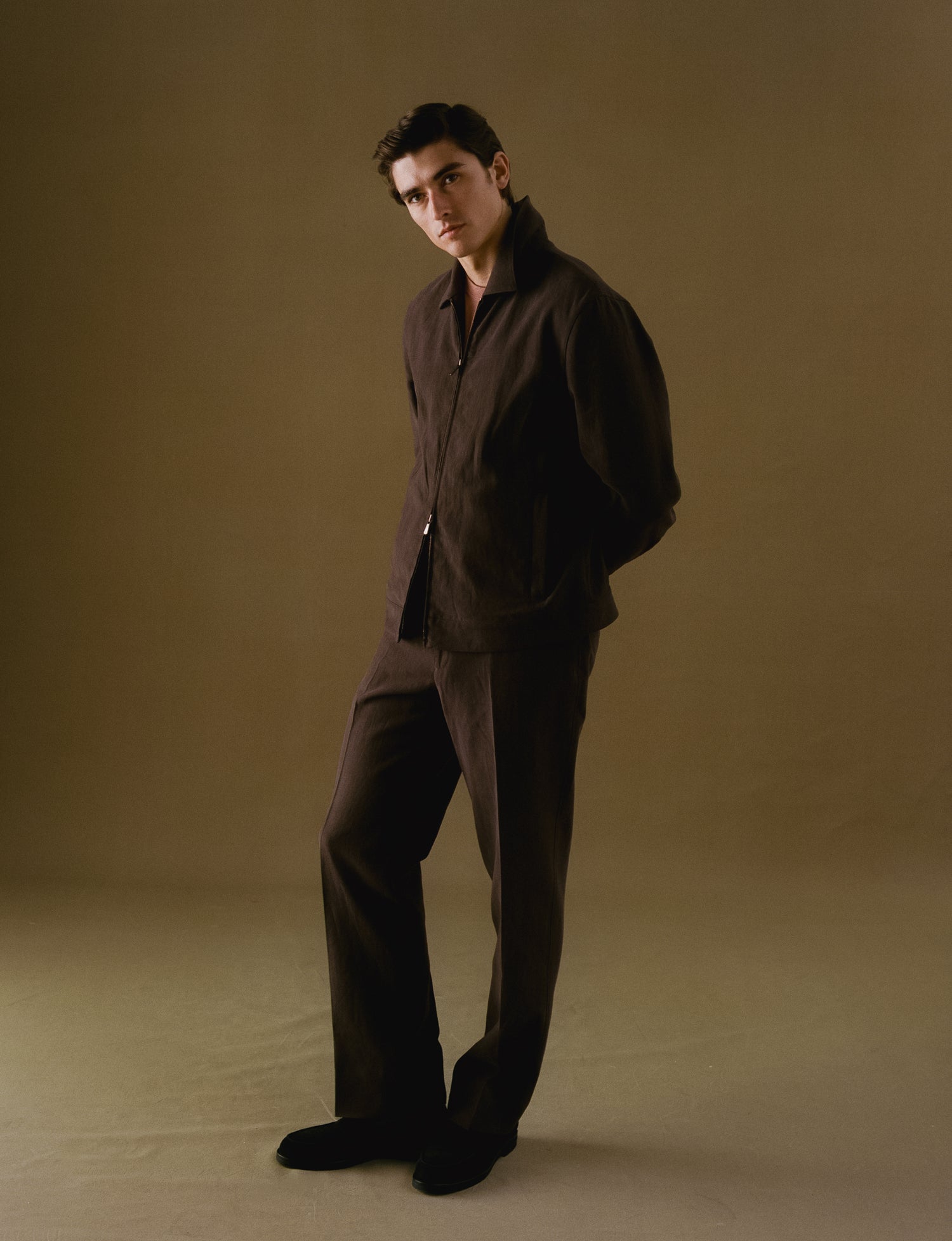 Man wearing a brown linen bomber and brown linen trousers against a beige background