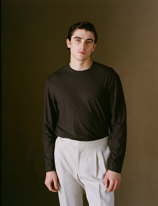 Man wearing a dark long-sleeve shirt over a white shirt against a brown background