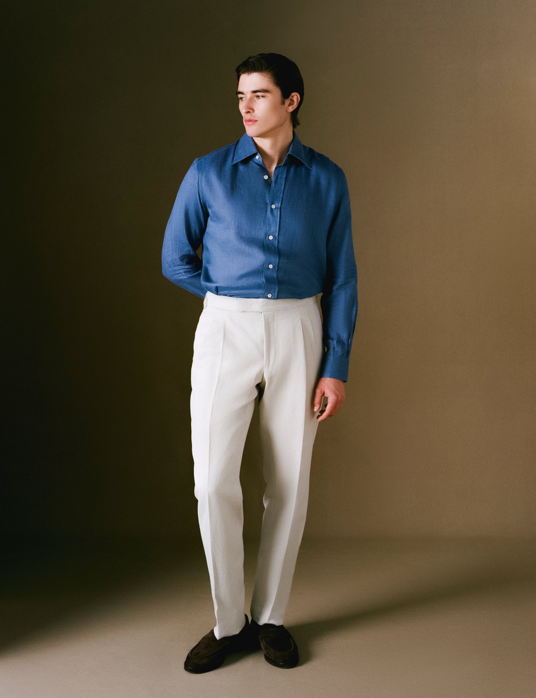 Man wearing a blue shirt and white pants against a brown background