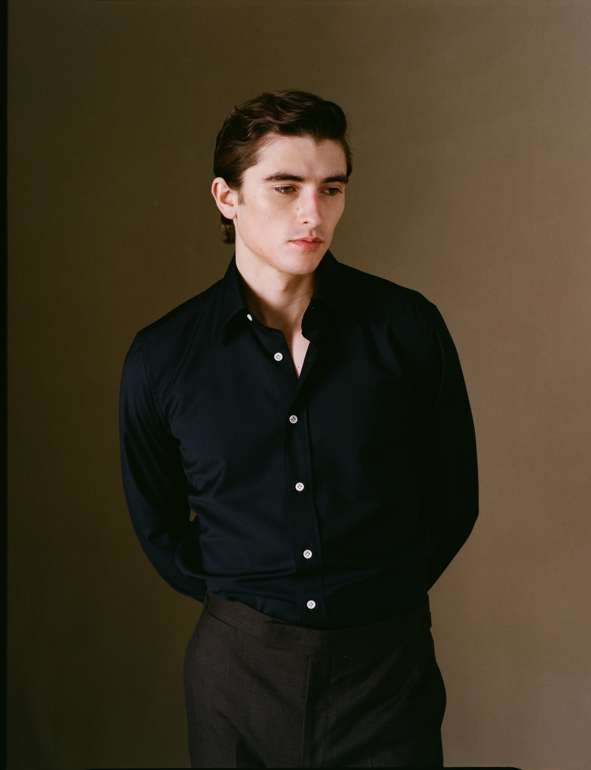 Man wearing a navy shirt with white buttons against a brown background