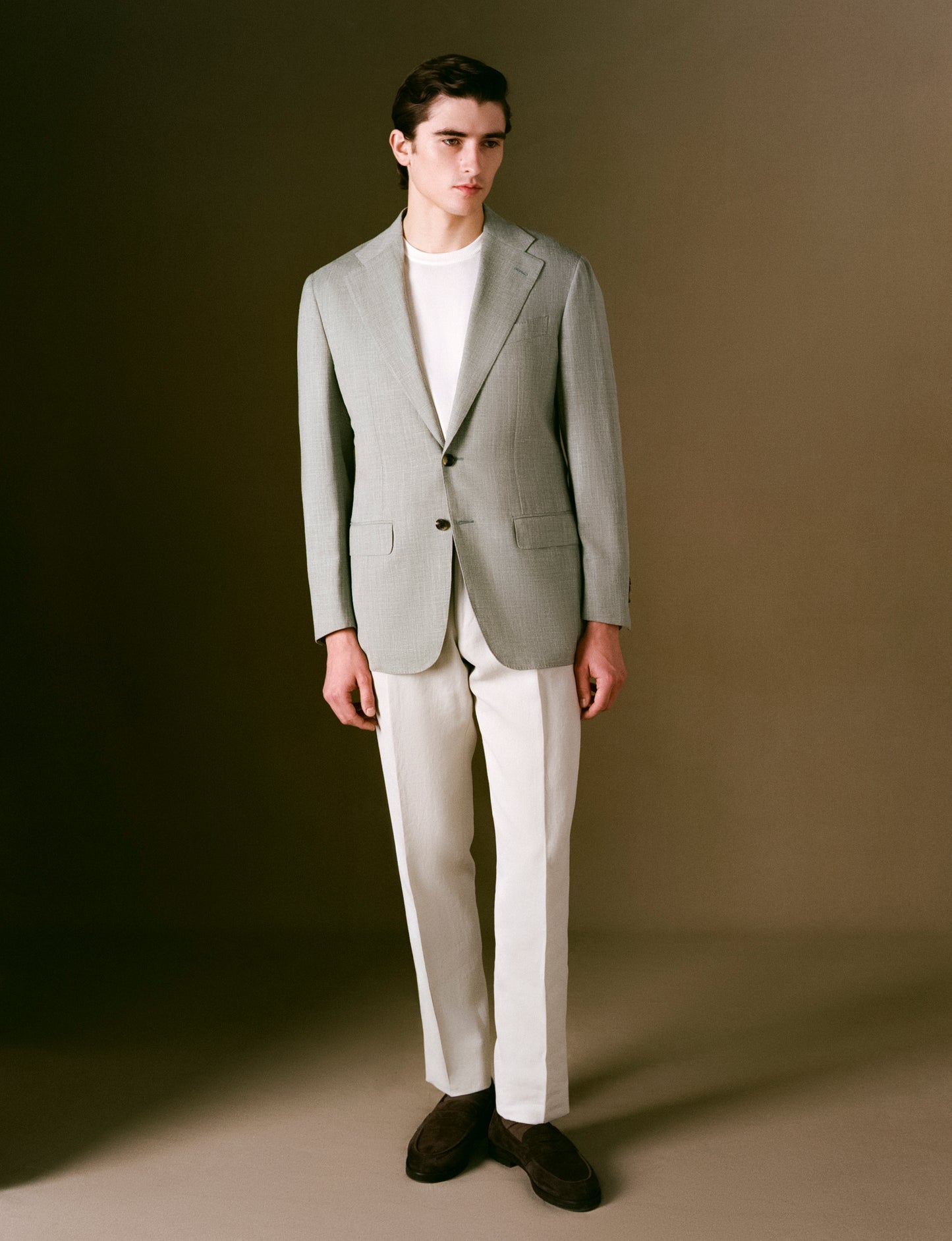 Model in a light sage suit jacket with a white shirt against a brown background