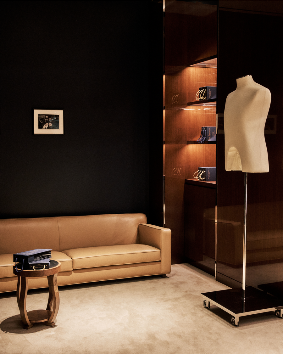 Modern interior with a brown leather sofa, small round table, and mannequin against a dark wall.