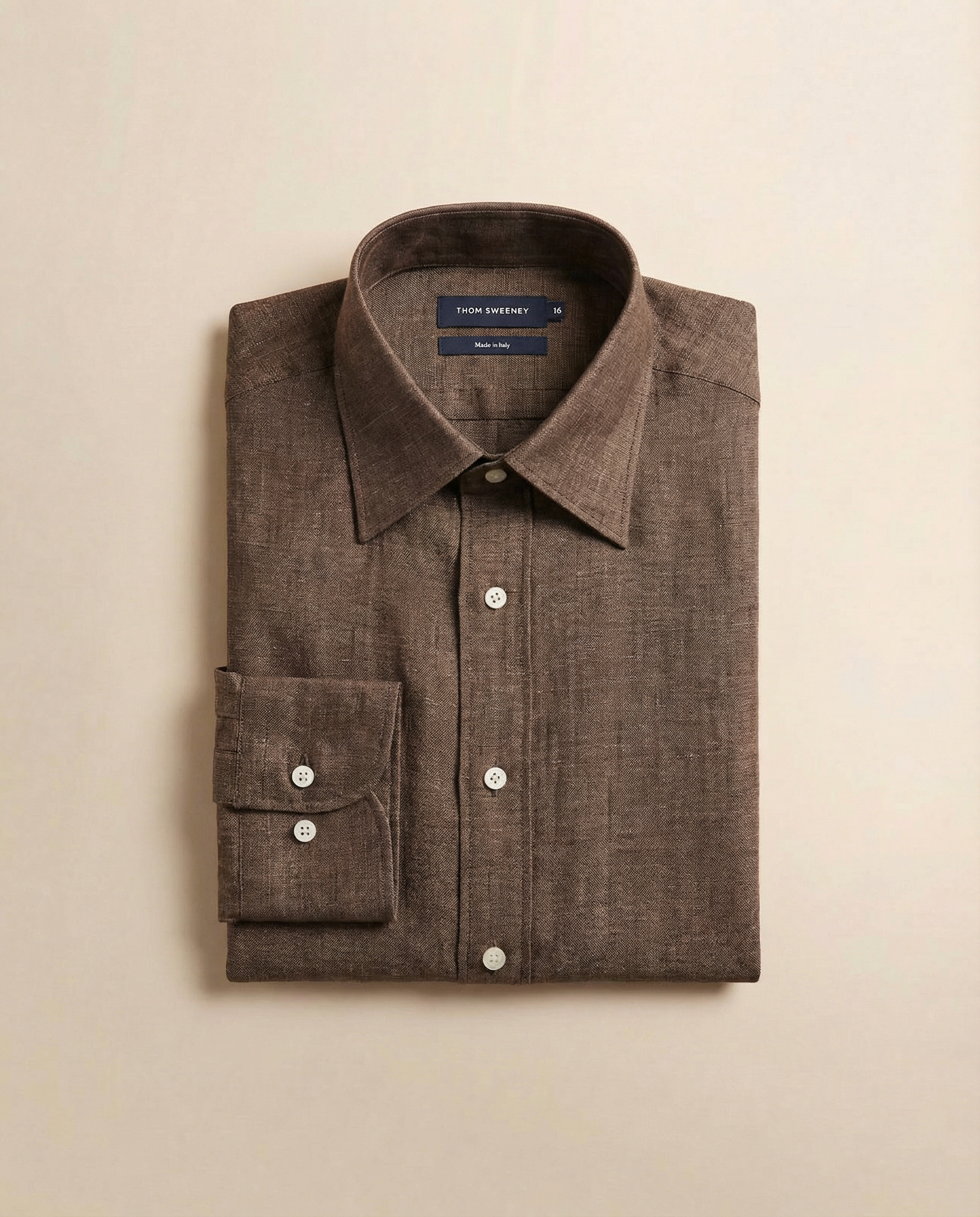 Folded brown dress shirt with a label on a beige background