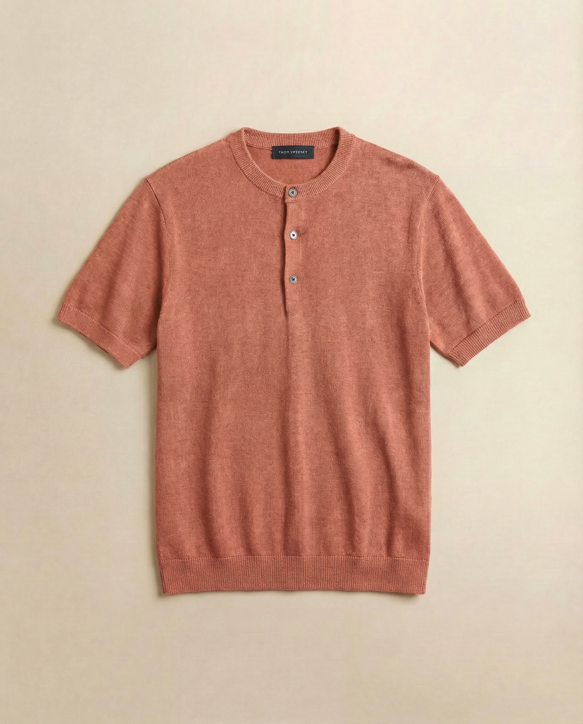 Salmon coloured short-sleeve sweater with button details on a beige background